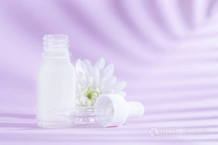 天然化妆品带滴管的精华液和淡紫色背景上的白花。