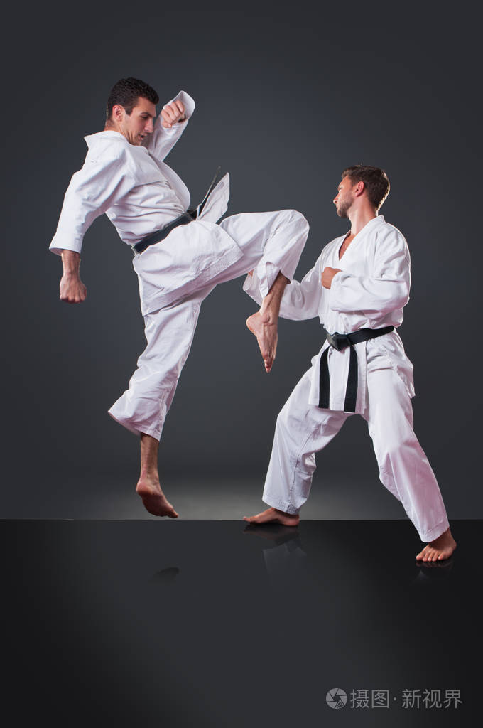 年轻英俊的男空手道运动员在灰色背景上踢球