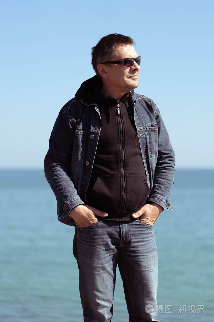春天阳光明媚的日子里,一个穿着牛仔服的男人站在海边的背景上.