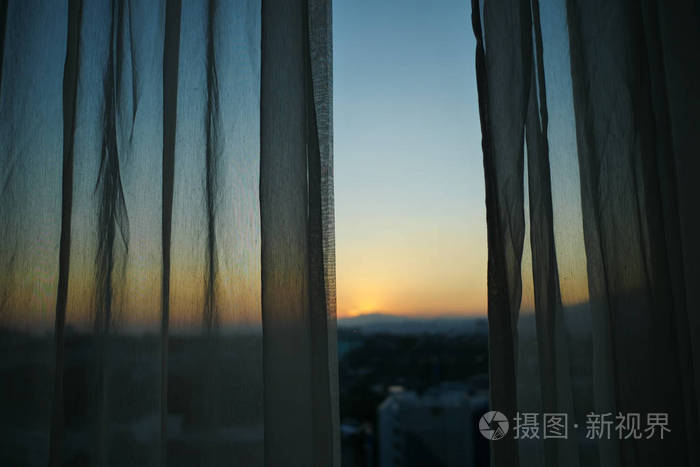 阳光透过白色窗帘窗外是夕阳的天空