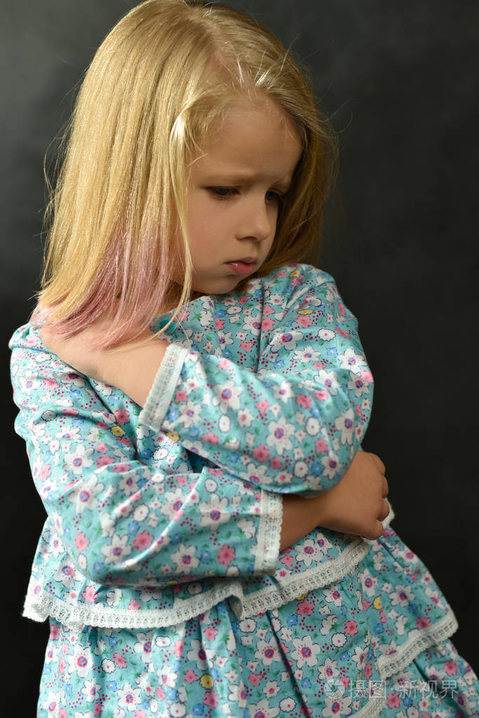 一个穿着裙子的小女孩站在黑色的背景上伤心哭泣