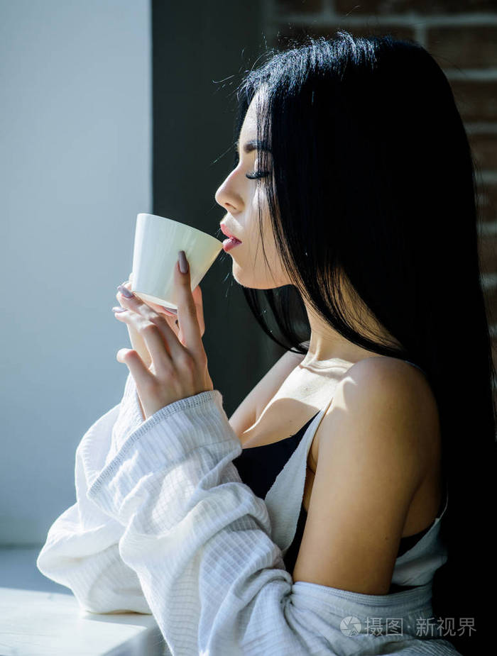 独自喝酒漂亮的女人在窗边喝着新鲜的热咖啡性感女孩喝着她最喜欢的