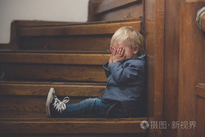 悲伤的孩子坐在一座大房子的楼梯上概念为不