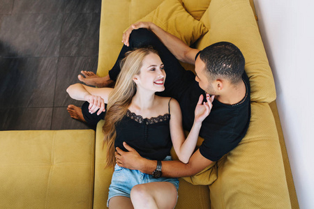 相爱的情侣拥抱在一起,躺在沙发上,看着对方.年轻女人摸男人的脸.