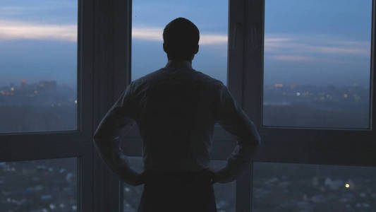 商人的背影站在窗边,看着夜市的背景照片
