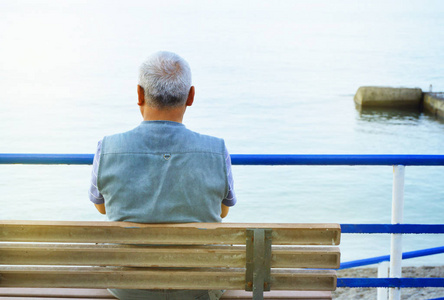 孤独的白发老人坐在海边的长凳上,从后面眺望,凝望大自然,享受一个