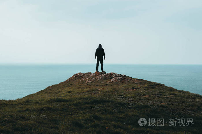 一个孤独的蒙面人站在山顶上眺望大海