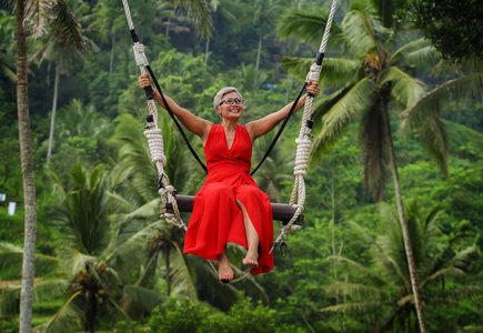 一头白发,穿着时髦的红裙子,骑着雨林荡秋千,无忧无虑地荡秋千照片