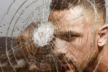 一个强壮的男人用拳头推倒玻璃墙.英俊的拉丁美洲男人透过碎玻璃看.