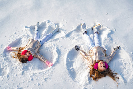 雪花秀logo两个小女孩躺在雪地上做雪天使.快乐女孩在雪地天使秀.照片