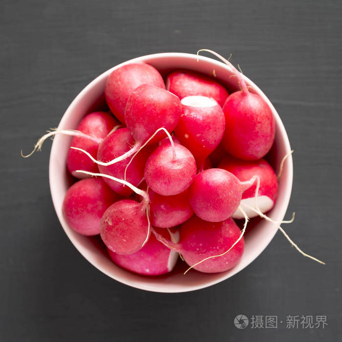 新鲜的红萝卜放在一个粉红色的碗里在黑色的背景上偷听