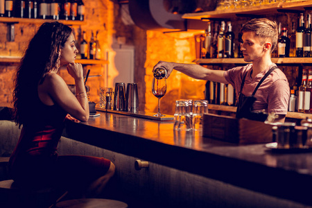 酒吧男招待为坐在吧台旁的女士倒红酒照片