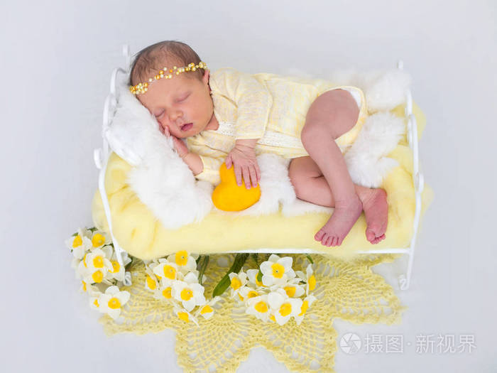 一个手拿着黄色装饰心脏的新生婴儿睡在床上。