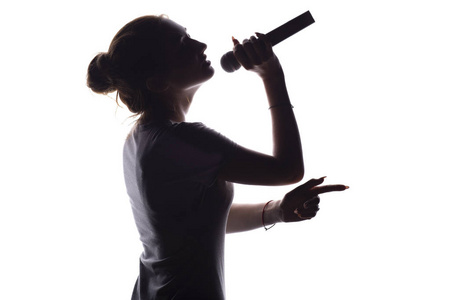 演唱背景表演女孩的剪影,对着麦克风唱歌,年轻女子的侧影在白色孤立的
