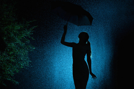 剪影少女的身影在雨中撑伞,一位年轻女子用手挑起头发,高兴地滴下水滴