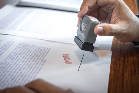 商人的手在书面文件上盖章以批准业务照片