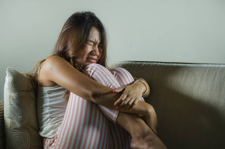 伤心分手年轻的印尼亚裔妇女,伤心沮丧,坐在家里的沙发上哭泣,沮丧和