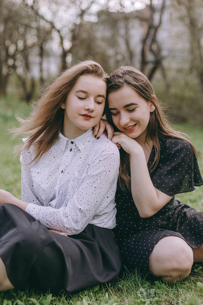 两个美丽的小妹妹坐在绿色的春天公园里在田野里拥抱