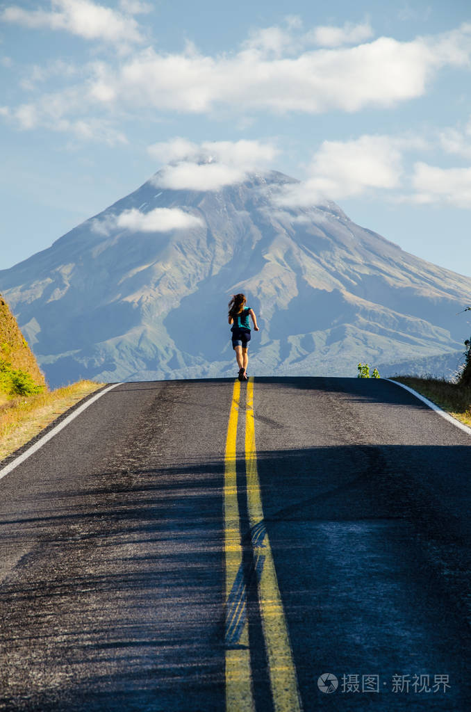穿着绿色t恤的跑步女孩在路上背景是塔拉纳基山上面是云层埃格蒙特