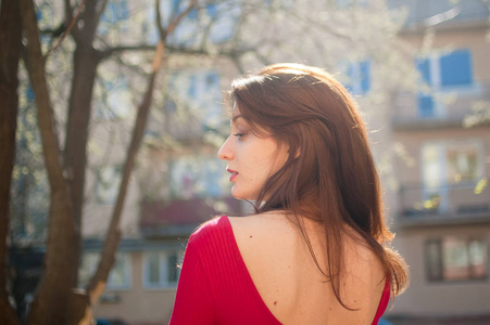 年轻的黑发女人的背影,吹着风吹的头发,性感的嘴唇和红色的衬衫在城市