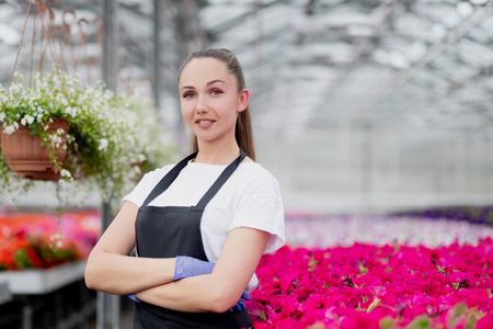 围裙工作服穿着工作服和围裙的迷人的年轻女性花匠或农艺师在大型玻璃