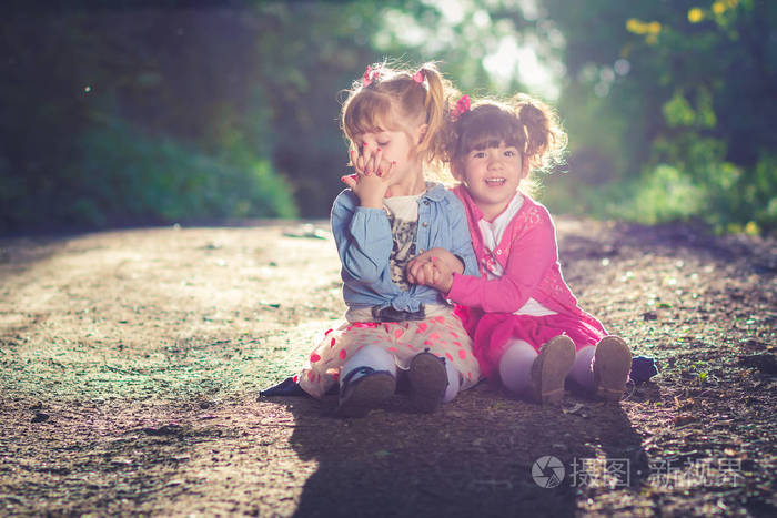 两个小女孩姐妹们穿着粉红色的裙子和小猪尾巴拥抱在一起