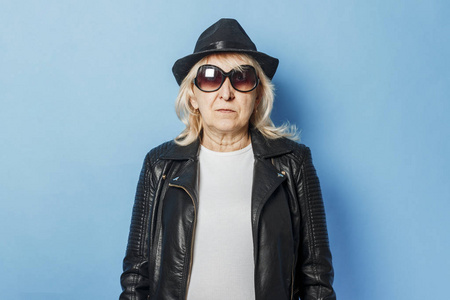 戴着眼镜,皮夹克,戴着帽子的老太太,背景是蓝色.