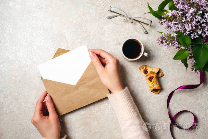 女人手拿着牛皮纸信封和空白卡片放在女人的办公桌上,上面装饰着咖啡
