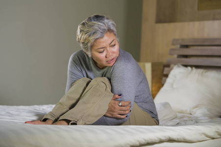 悲伤和失落的中年妇女灰色头发坐在床上感到沮丧,遭受抑郁和痛苦照片