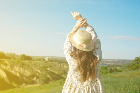 身着夏装,头戴草帽的黑发女郎,正站在高高的草丛中,双臂高举,面向阳光