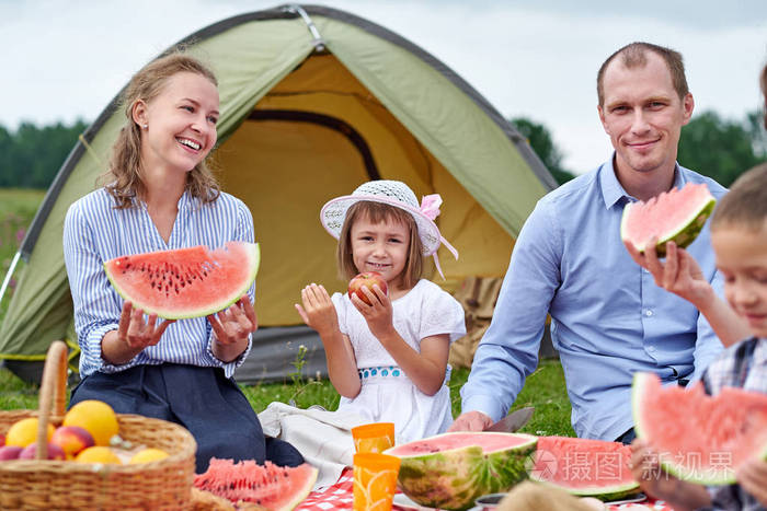 快乐的一家人在帐篷附近的草地野餐吃西瓜妈妈爸爸和孩子在乡下野营