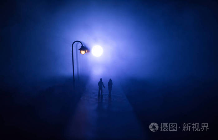 一对年轻夫妇手牵着手夜晚在白色的路灯下慢慢地走着黑暗时期雾中宁静