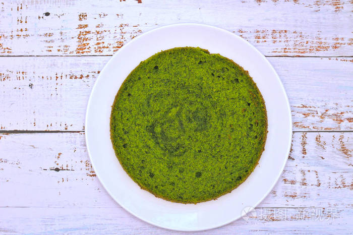 绿色圆形菠菜薄荷蛋糕放在一个白色盘子里放在破旧的木板上