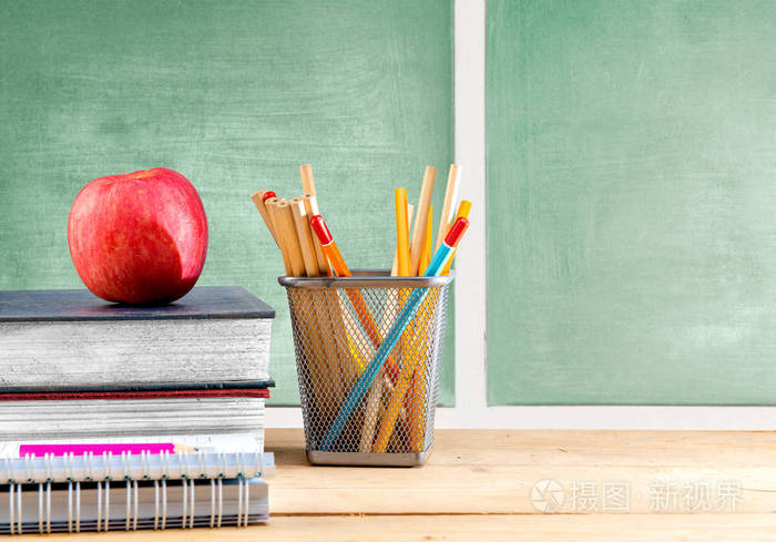 一堆放着苹果和铅笔的书放在木制的篮子里