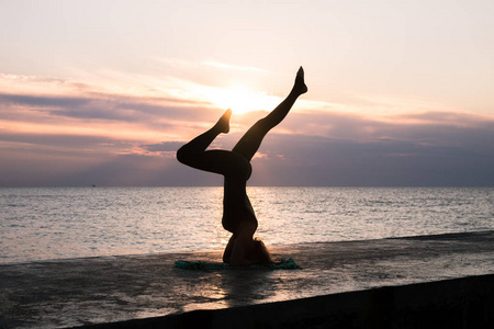 无法辨认的女子,美丽的身体做瑜珈头倒立在日出的海上,瑜伽姿势的剪影