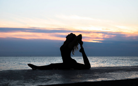 剪影一位身材美丽的女士在海上日出时做瑜伽劈叉,瑜伽姿势的剪影照片