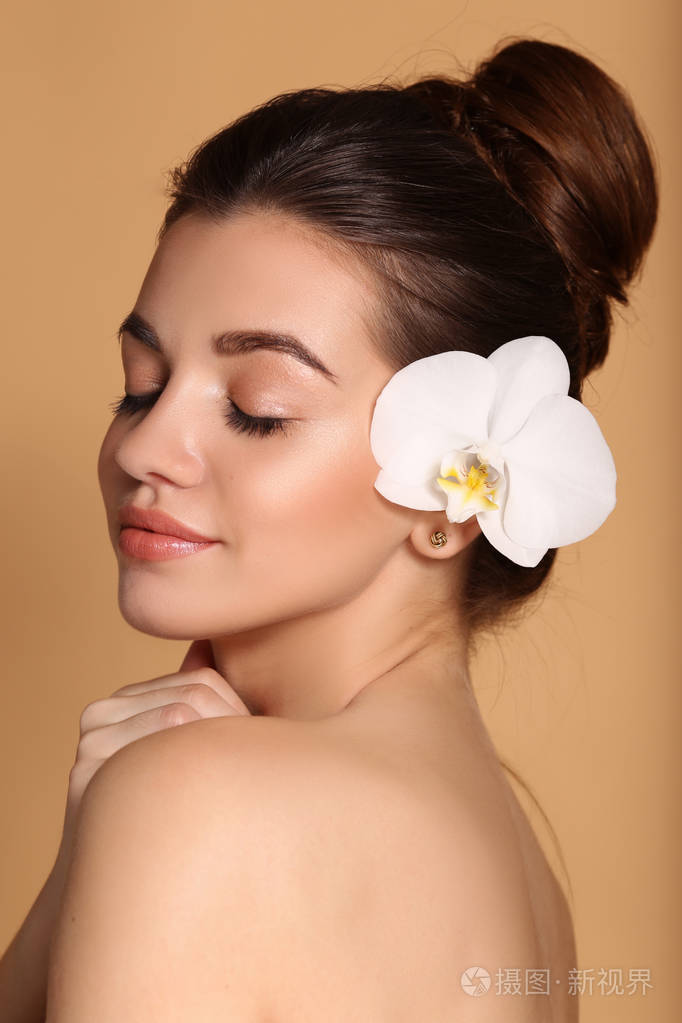 年轻美丽的女孩皮肤完美无瑕双手捧着白色的兰花护肤美容和化妆品概念