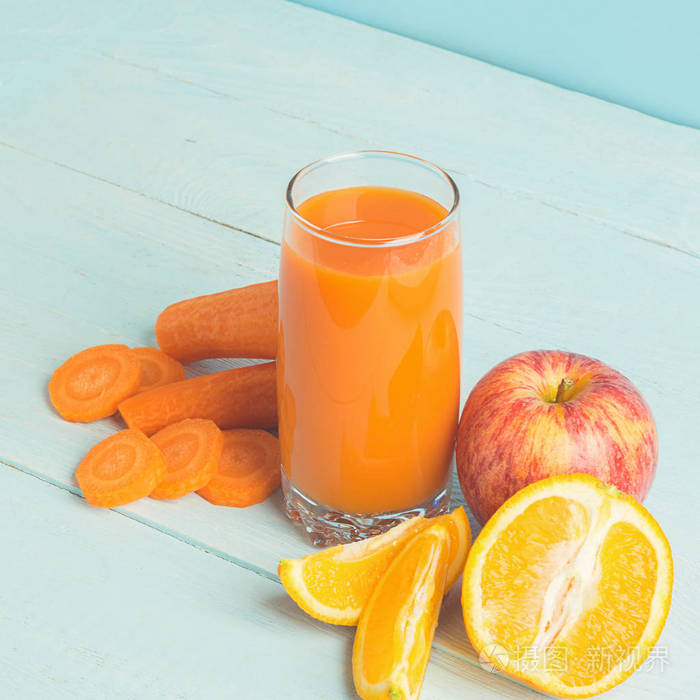 新鲜的果汁从胡萝卜和橙子苹果在一个木制的蓝色背景玻璃选择性聚焦