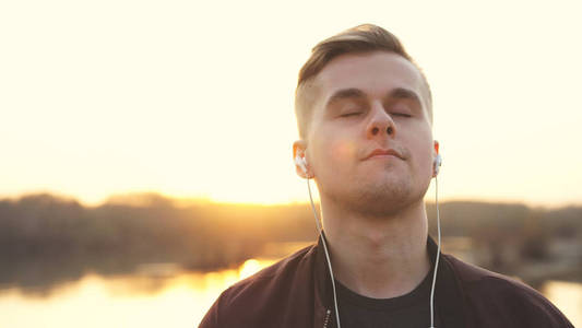 沙滩的高清背景日落时,一个闭着眼睛的年轻帅哥在沙滩上听音乐.照片