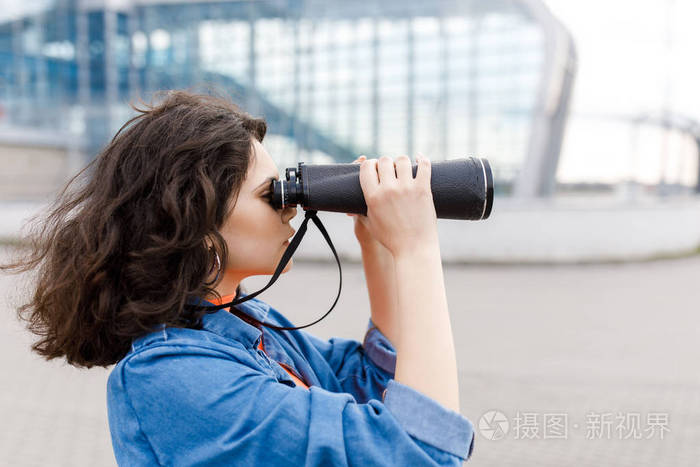 年轻漂亮的女孩手里拿着双筒望远镜看向别处这个年轻人旅行