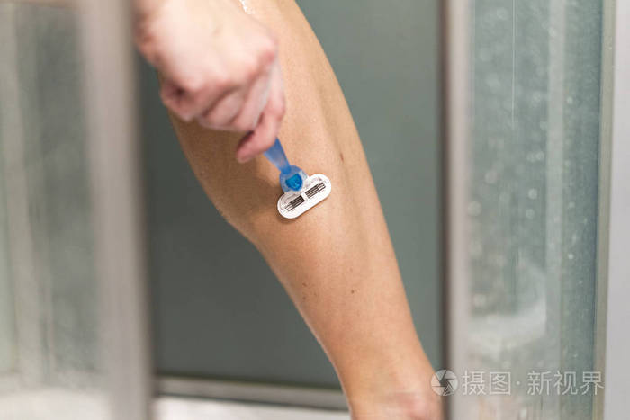 性感的年轻女人在浴室里刮腿毛.使用剃须刀的女性腿部特写镜头.