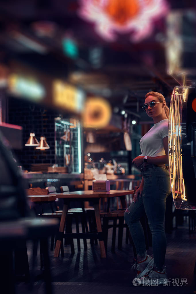 在霓虹灯酒吧一位戴着墨镜的迷人女子正在为摄影师摆姿势