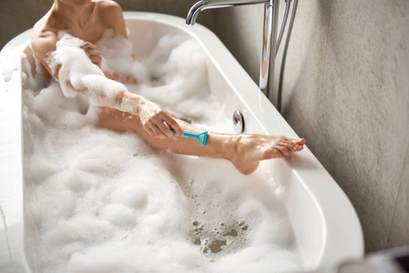 年轻女士在泡沫浴中刮腿毛图片