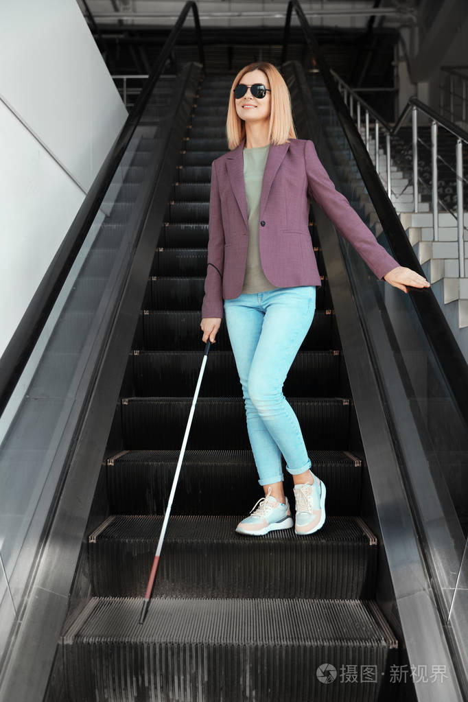 室内自动扶梯上带长拐杖的盲人