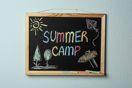 小黑板上有文字夏令营,图画和粉笔挂在彩色墙上照片
