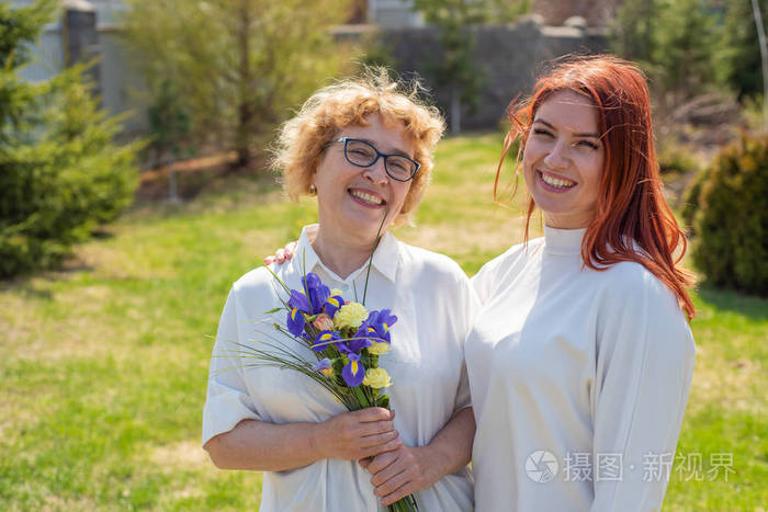 成年女儿在屋外的院子里给母亲送花一起度过时光周末在家庆祝母亲节