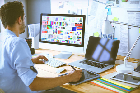 年轻设计师在线工作时,坐在电脑和电脑前的画室里.照片