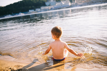 河里游泳孩子主题是夏季，在水边休息。快乐的白人小男孩在河里玩耍和享受。孩子正在湖塘沙滩上休息和游泳照片