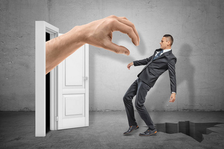 一只大手从白色的门口伸过去,抓住了正掉在地上的年轻商人,背景是灰色