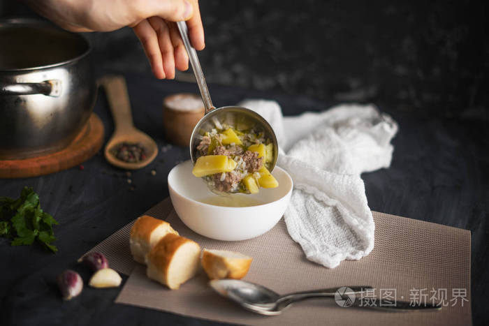 厨师用手将新鲜的热汤倒在一个白色的空碗里准备食物